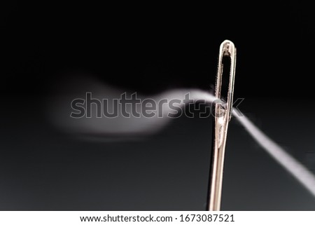 Needle with white thread threaded on black background