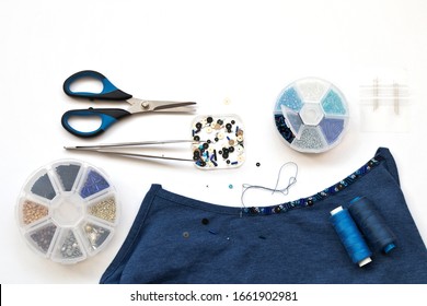 Needlework and beadwork. Decoration of a blue top with bugle embroidery, bead and sequins. Accessories for embroidery: sets of beads in boxes, tweezers, needles and scissors on a white background