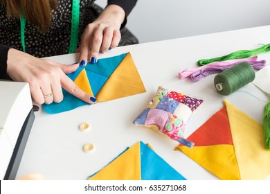 Needlework And Quilting In The Workshop Of A Young Woman, A Tailor - Close-up On Hands Of A Tailor With Scraps Of Colorful Fabrics Lying On A White Table Buttons, Pins, Pin Cushion