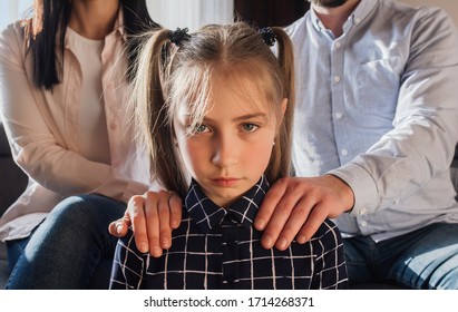 needs of upset girl on background of parents. They put their hands on her shoulders. She has big and sad eyes.