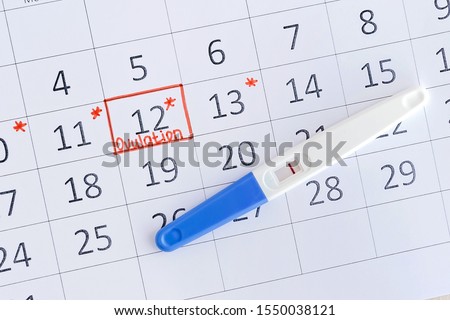 Negative pregnancy test with circling date in calendar. Planning of pregnancy, trying to have baby. Top view.