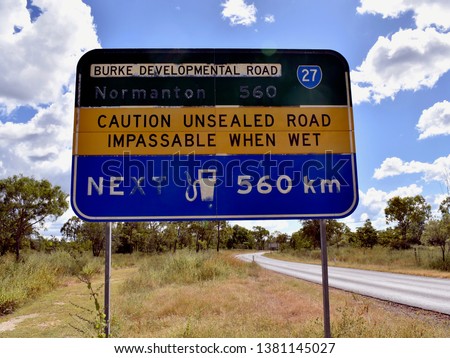 A neglected sign in outback Australia indicating an unsealed road with next fuel station 560 kilometers away