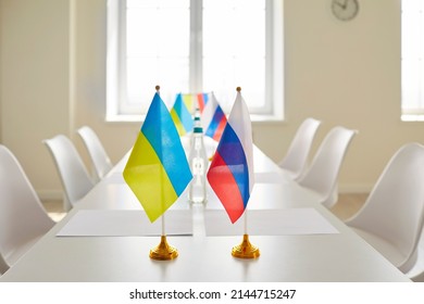 Negotiation Between Ukraine And Russia. Close Up Of Ukrainian And Russian Flags Standing On Long Table With Chairs In Empty Meeting Room. Concept Of Conflict Resolution In Ukraine.