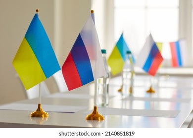 Negotiation Table With Water Bottles And Flags Of Ukraine And Russia In Empty Office Room After Diplomatic Meeting Aimed At De-escalation, Ending War And Peace Restoration. Close Up. Nobody, No People