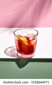 Negroni-Cocktail auf rosafarbenem Hintergrund. Trinken Sie bei Tageslicht in Roxglas mit hartem Schatten aus Palmblättern. Konzept des Sommers, tropischen und frischen Getränks.