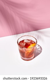 Negroni Cocktail Over Pink Background. Drink In Rox Glass In Daylight With Palm Leaf Hard Shadow. Summer, Tropical, Fresh Drink Concept.