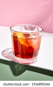 Negroni-Cocktail auf rosafarbenem Hintergrund. Trinken Sie bei Tageslicht in Roxglas mit hartem Schatten aus Palmblättern. Konzept des Sommers, tropischen und frischen Getränks.