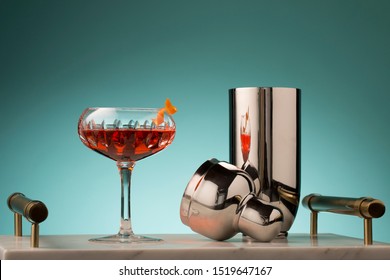 Negroni Served In A Crystal Coupe Glass With A Twist Of Orange. Shot On A Teal Background And Placed Upon A Marble Serving Tray