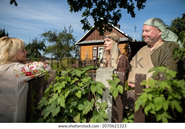 Neighbors chat with smiles on their faces while\
standing by an old wooden\
fence.