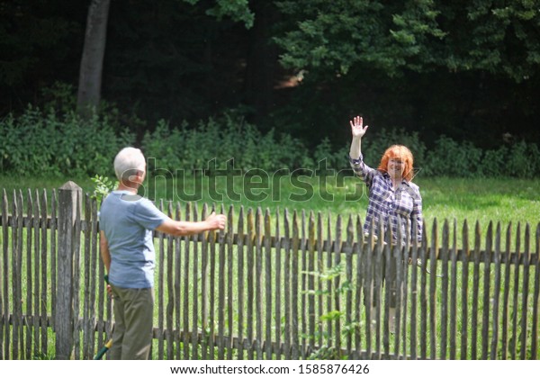 Neighbors greeting each\
other over fence