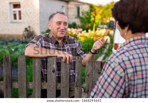 neighbors middle aged man and woman chatting near\
the fence in the\
village