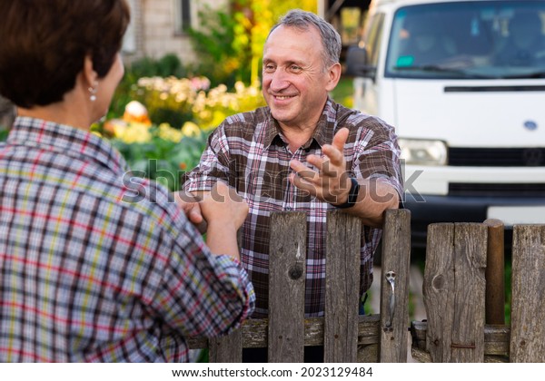 neighbors middle aged man and woman chatting near\
the fence in the\
village