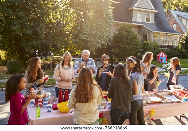 Neighbours\
talk and eat around a table at a block\
party
