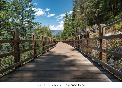 Nelson, British Columbia, Canada.  Two People Riding Bicycles Over One Of The Trestle Bridges Along The Burlington Rail Trail / Great Northern Rail Trail / Great Northern Trail In Summer.