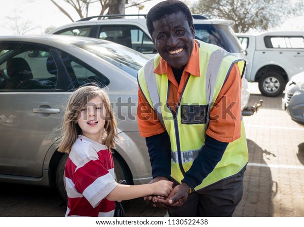NELSPRUIT, SOUTH AFRICA – JULY 30, 2013:\
A young white girl tips a friendly black security car park\
attendant.  Car guards are prevalent in South Africa and have\
controversial\
self-employment.