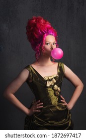 Neo Kitsch, Young Woman In Baroque Style, Costume And High Hairstyle In Historical Style And Modern Elements. Pink Hair And A Bubble Of Pink Gum, Old And New Concept