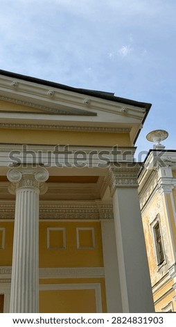 Neoclassical building exterior with ionic column capital, decorated pediment and roof sculpture.