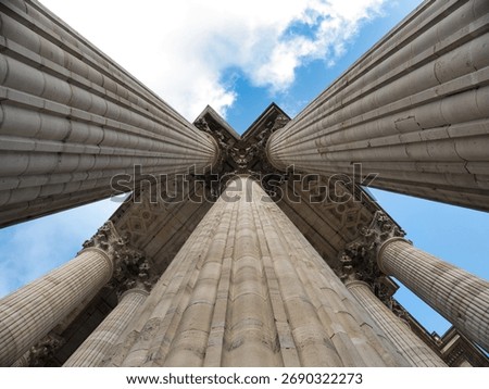 Neoclassical Columns from Low Angle Perspective - Dramatic low-angle view looking straight up between monumental fluted stone columns towards a richly decorated ceiling and a bright blue, cloudy sky.