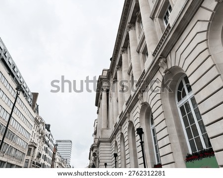 Neoclassical facade with grand columns frames a London, UK street scene beneath a soft overcast sky.