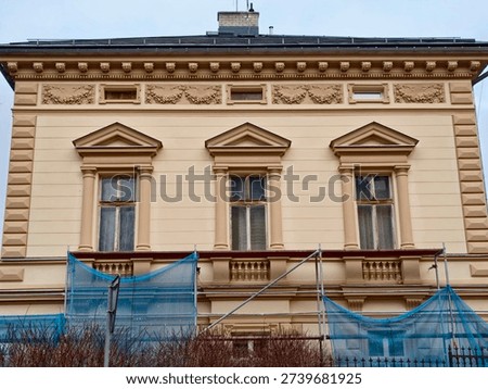 Neoclassical facade scaffolding netting at base, cornice detail and sash windows, restoration in progress