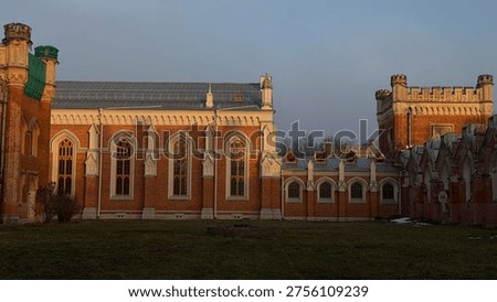 Neo-gothic red brick palace facade glowing in golden hour sunlight. Pointed arch windows, white trim, and decorative towers stand against a clear sky.
