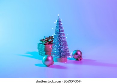 Neon Christmas winter background. Minimal abstract tree, xmas gift box. Holiday decoration bauble ball on neon gradient backdrop. Happy new year copy space - Powered by Shutterstock