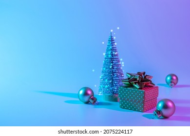 Neon Christmas winter background. Minimal abstract tree, xmas gift box. Holiday decoration bauble ball on neon gradient backdrop. Happy new year copy space - Powered by Shutterstock