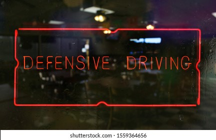 Neon Defensive Driving Sign in Wet Window of Restaurant