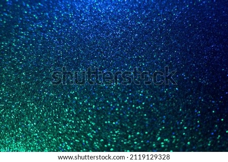 Neon glitter background. Grain texture. Defocused sparkles. Bokeh glow. Fluorescent blue green color gradient light shimmering round sequin pattern.