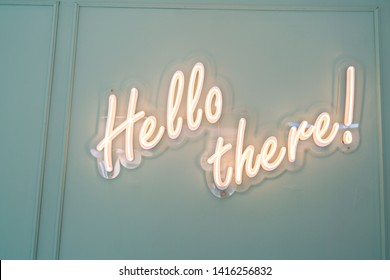 Neon glowing sign with word Hello there and green wall.