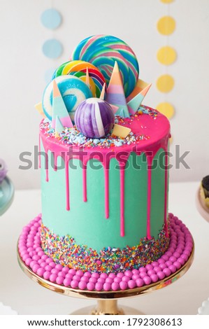Neon green and pink drip happy birthday cake by Katherine Sabbath topped with assorted rainbow coloured lollipop swirls and candy shards