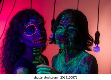 Neon Halloween Make Up For Day Of The Dead Celebration In Mexico. Ultra Violet Neon Portrait Photography With Two Hispanic Girls. 