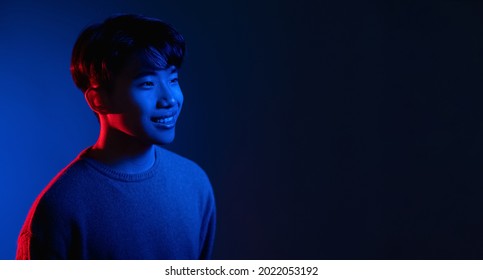 Neon Light Man. Cyberpunk Banner. Happy Smile. Positive Emotion. Portrait Of Cheerful Asian Guy In Bright Colorful Shining Red Blue Glow Isolated On Dark Empty Space Background.