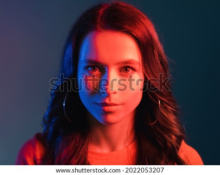 Neon light people. Retro wave portrait. Split personality. Hot and cold. Pretty smiling young woman face in bright colorful red blue glow isolated on dark background.