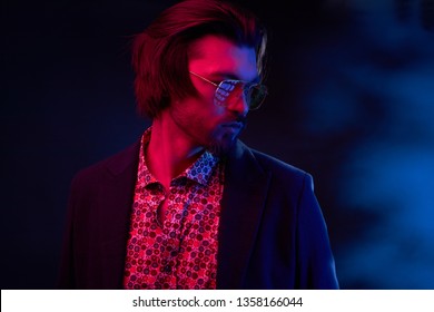 Neon Light Portrait Of Handsome Male Model With Dark Medium Length Hair, Mustaches And Beard In Sunglasses, Weared In Dark Jacket And Floral Shirt.