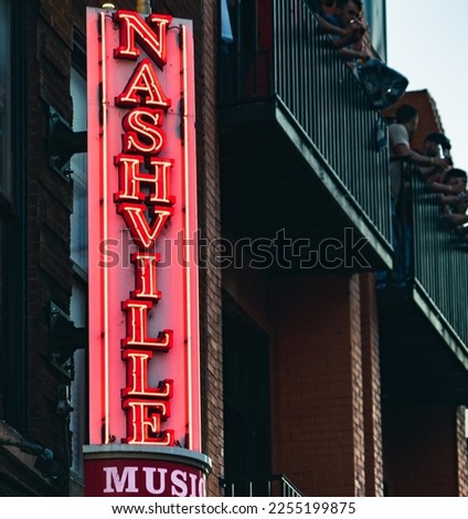 Neon music sign in downtown Nashville, Tennessee with people cheering on bar balcony