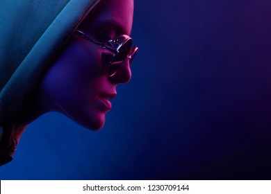 Neon Profile Portrait Of Young Woman In Sunglasses And Hoodie. Studio Shot With Smoke In Scene. 