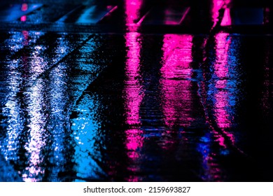 Neon reflection from street asphalt with pedestrian walking by. Futuristic city and cyberpunk concept.