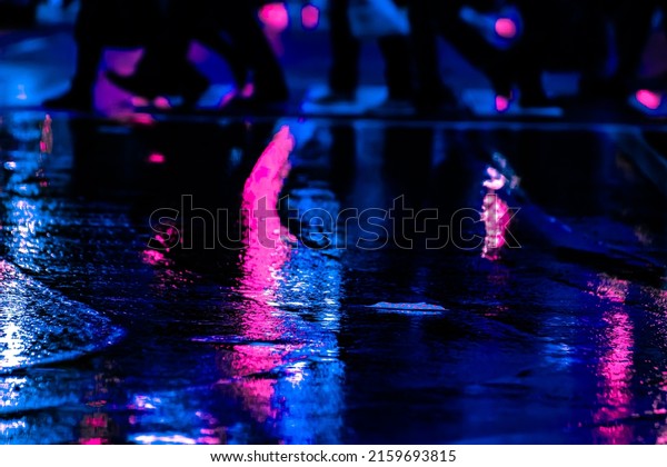 Neon reflection\
from street asphalt with pedestrian walking by. Futuristic city and\
cyberpunk concept.