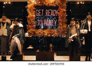 Neon shiny holiday signboard on boutique showcase with text Get ready for party and female mannequins