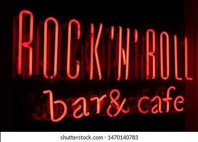 Neon Sign Glowing At Night Behind Glass: Rock ’N’ Roll Bar & Cafe.