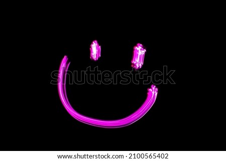 Neon smiling face, light painting pink smiling face against black background. Face expressions emoji.