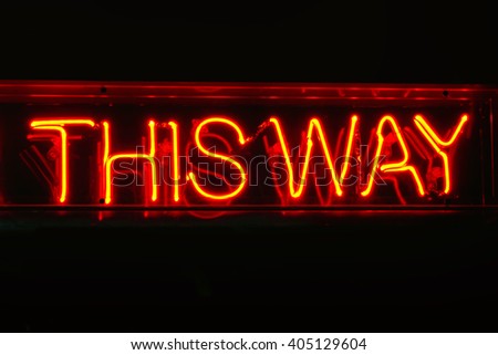 Neon THIS WAY sign; genuine traditional neon sign reading This Way; isolated on black ground
