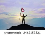 Nepal flag being waved by a man celebrating success at the top of a mountain against sunset or sunrise. Nepal flag for Independence Day.