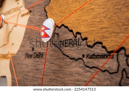Nepal flag on the pushpin with red thread showed the paths of movement or areas of influence in the global economy on the wooden map. Planning of traveling or logistic concept. Network connection. 