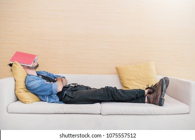 Nerd man sleep on sofa with book cover his face, sleep late reading book prepare for exam. Lifestyle education concept - Shutterstock ID 1075557512