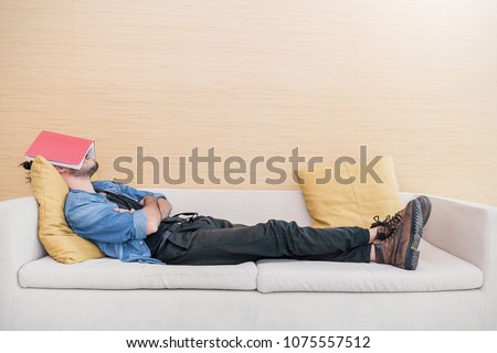Nerd man sleep on sofa with book cover his face, sleep late reading book prepare for exam. Lifestyle education concept