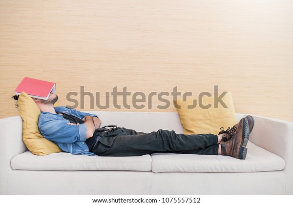 Nerd man\
sleep on sofa with book cover his face, sleep late reading book\
prepare for exam. Lifestyle education\
concept