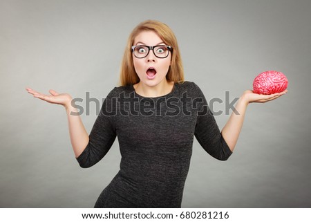 Nerdy shocked woman in big eyeglasses having confused face expression pointing with palm open hand and holding brain