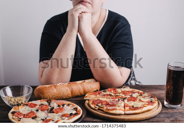 Nerve food,\
addiction, eating disorders, bulimia. Overweight woman sit at the\
table with big amount of junk\
food